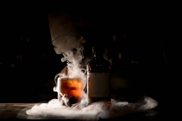 Beautiful old-fashioned glass of cocktail and bottle in dark bar with wonderful white smoke around stock photo