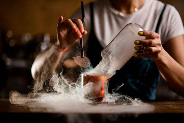 view of glass with cocktail that bartender decorates with plant leaf. Dry ice effect. stock photo