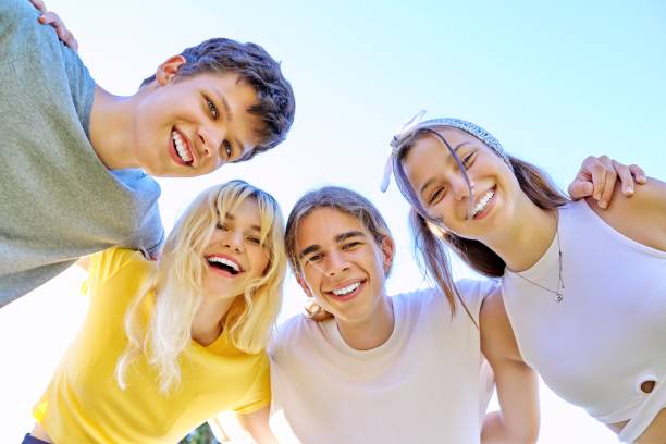 Close-up of happy smiling teenage faces. Hugging teenagers looking at the camera, sky background. stock photo