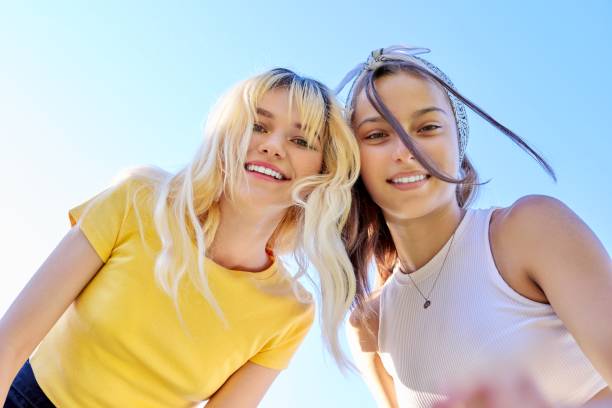 Close-up of happy smiling faces of teenage girls Close-up of happy smiling faces of teenage girls. Two females, blonde and brunette looking at the camera, sky background. cute 15 year old girls stock pictures, royalty-free photos & images