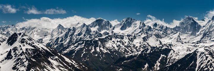 Snowy peaks of the Caucasus Mountains against a background of blue sky and white clouds
