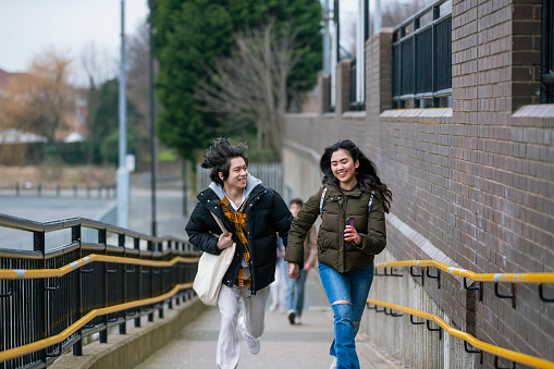 A close-up front-view shot of a teenage couple running up a concrete ramp while holding hands in Wallsend, North East England. They are trying to catch the next train on the Subway.