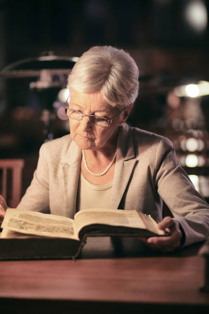 istock Senior woman reading in library at night 1327429966