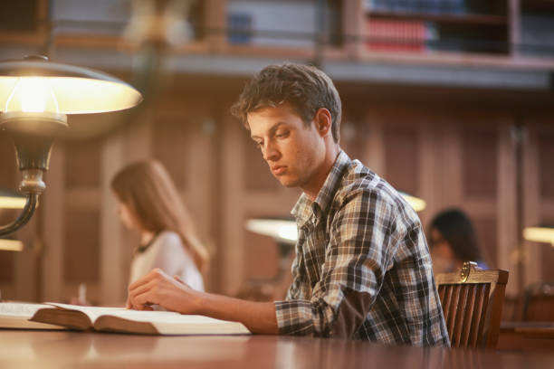 istock Young man reading in library at night 1327429974