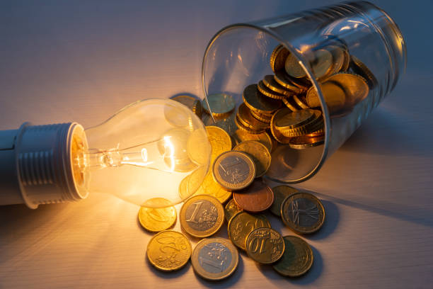 Light bulb lit with glass full of coins next to it. stock photo