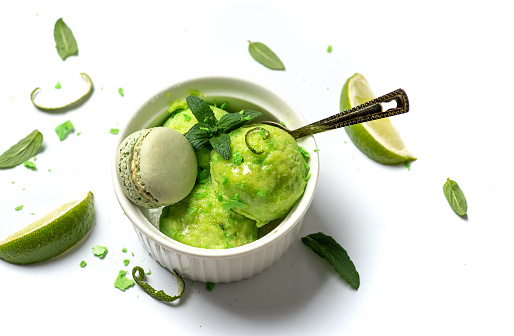 Homemade green organic lime fruit ice cream balls with mint leafs served in a cup on white background top view. Cold and refreshing organic dessert for the summer