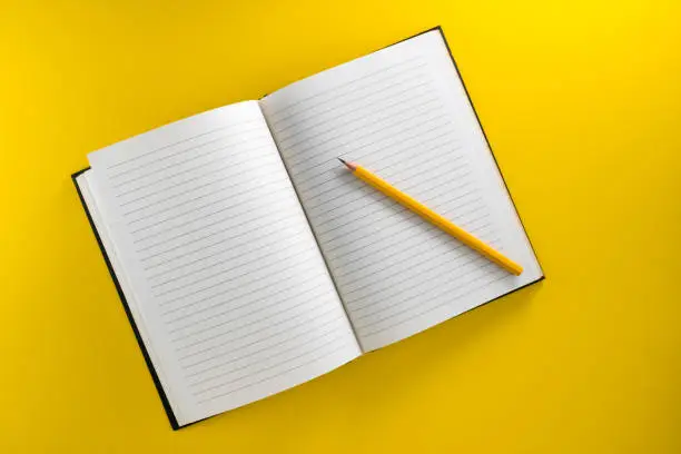 Photo of notebook with yellow pencil isolated on yellow