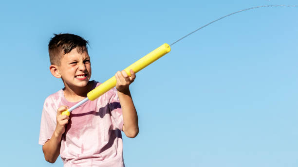 gioco estivo per bambini, guerra d'acqua. primo piano ritratto bambino bambino che gioca con pistola ad acqua nella calda giornata estiva, spara con pistola giocattolo sullo sfondo del cielo blu. baner, spazio di copia - toy gun foto e immagini stock