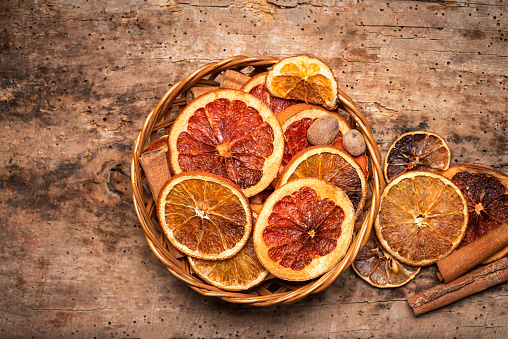 Dried sliced orange and grapefruit fruit slices in a wicker bowl tabletop rustic view