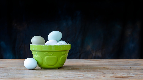 Close up of a bowl of eggs sitting on a table in front of a black background.
