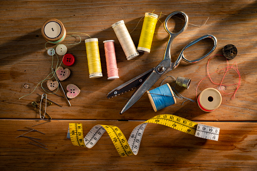 Direct above shot of scissors, measuring tape, threads and buttons on a table.