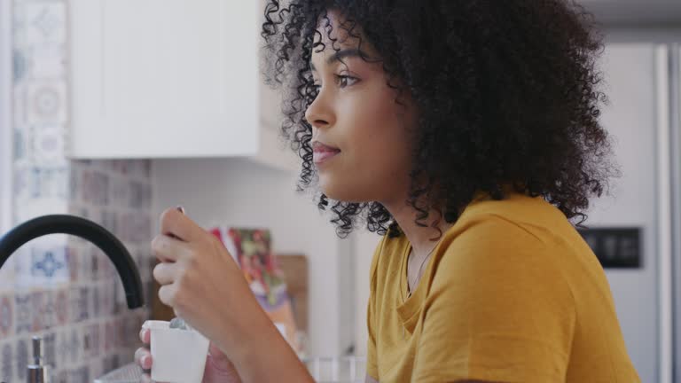 Shot of a young woman eating yogurt in the kitchen