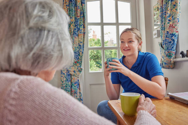 weibliche haus hilfe mit tasse tee mit einsamen senior frau in der küche - community outreach home caregiver care cheerful stock-fotos und bilder