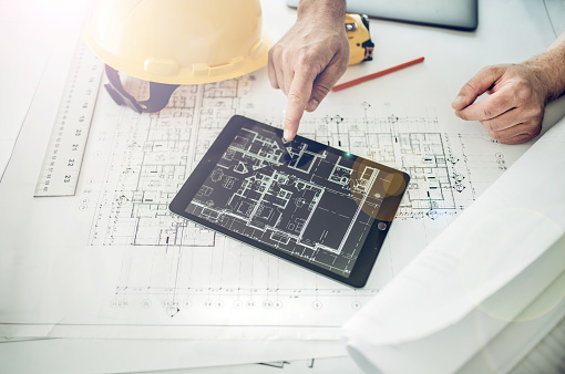 Hands of an architect, engineer or a site superintendent pointing at the architectural plan on a tablet computer.