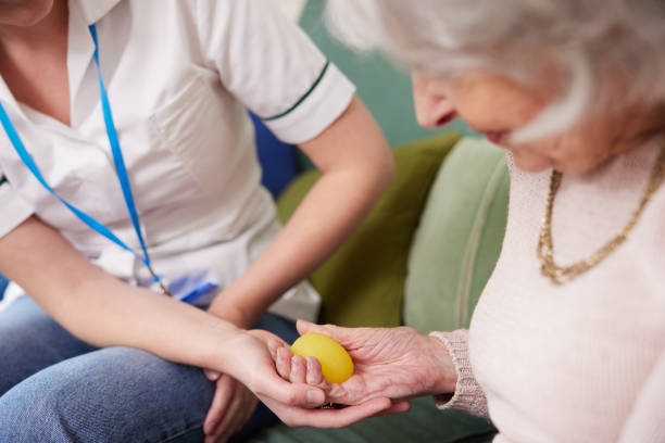 fisioterapeuta femenina conseguir mujer mayor para exprimir la pelota de goma en casa - occupational therapy fotografías e imágenes de stock