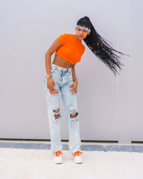 un jeune danseur de trap aux tresses. black grind girl de l’ethnie africaine avec t-shirt orange et pantalon de cow-boy sur fond gris, tresses mouvantes et souriant - us supreme court photos et images de collection