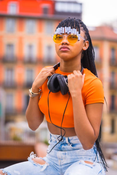 street style d’un jeune danseur de trap avec des tresses. elle pose de la fille noire grinçante du groupe ethnique africain avec une chemise orange et un pantalon de cow-boy assis. avec fond de maisons orange - us supreme court photos photos et images de collection