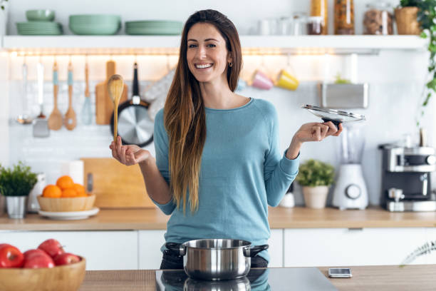 glückliche junge frau kochen gesundes essen in auflauf, während es zur kamera in der küche zu hause aussät. - smart casual occupation casual healthy eating stock-fotos und bilder