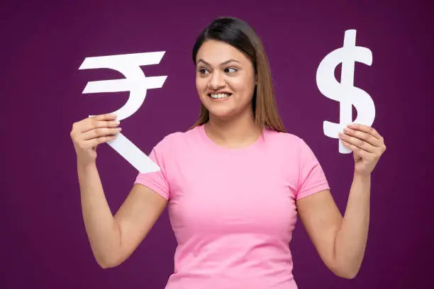 Photo of Portrait of young women showing dollar sign and Indian currency symbol standing isolated over purple background:- stock photo