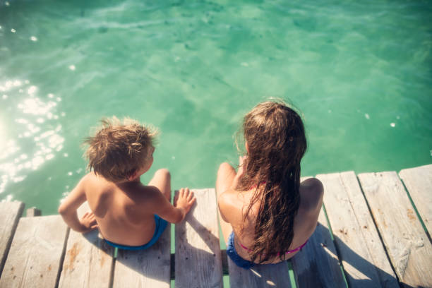 istock Summer vacations - brother and sister sitting on on pier 1327456863