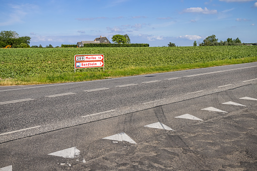 Road signs in front of a field with sugar beets and an farmhouse on Lolland, a large island in Denmark which is famous for its sugar industry