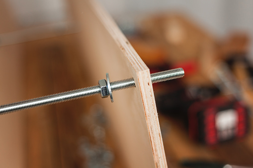 Furniture making, threaded steel rod with plywood plate, close up detail, selective focus