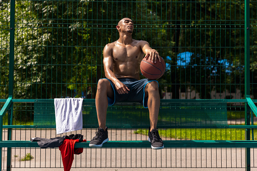 Waiting for game, team. Young strong man, male basketball player practicing at street public stadium, sport court or palyground outdoors. Concept of healthy active lifestyle, motion, hobby.