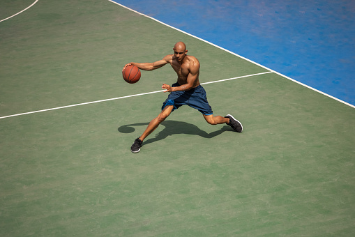 High angle view of young man, male basketball player playing basketball at street public stadium, sport court or palyground outdoors. Concept of healthy active lifestyle, motion, hobby.