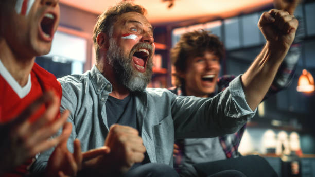 à la maison, trois fans de sport joyeux avec des visages peints assis sur un canapé regardent un match à la télévision, célèbrent la victoire lorsque l’équipe sportive gagne le championnat. amis applaudir, crier. portrait tourné - sport games photos et images de collection