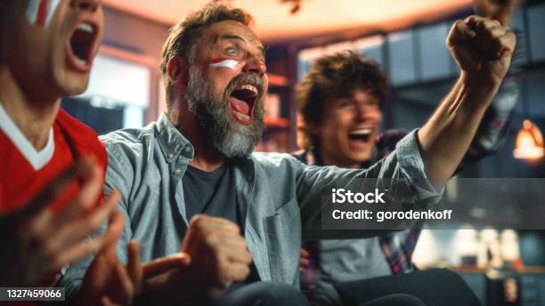 At Home Three Joyfuls Sports Fans With Painted Faces Sitting On A Couch Watch Game On Tv Celebrate Victory When Sports Team Wins Championship Friends Cheer Shout Portrait Shot Stock Photo - Download Image Now