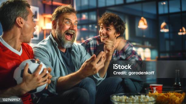 Night At Home Three Soccer Fans Sitting On A Couch Watch Game On Tv Use Smartphone App To Online Bet Celebrate Victory When Sports Team Wins Friends Cheer Eat Snacks Watch Football Play Stock Photo - Download Image Now