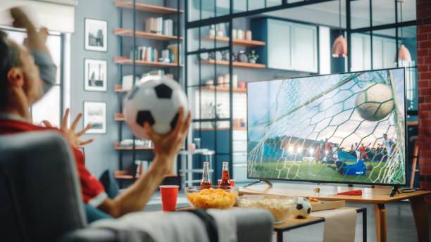 en casa los fanáticos del fútbol sentados en un sofá ven el partido de fútbol en la televisión, animen al equipo de deportes de favortis para ganar el campeonato. la pantalla muestra el juego del club de fútbol profesional. sobre el hombro - sport watching television broadcasting television fotografías e imágenes de stock