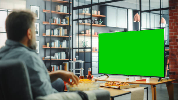 w domu człowiek siedzi na kanapie watch green screen chroma key tv. w średnim wieku mężczyzna odpoczywanie, zegarki show, wydarzenie sportowe, film, na żądanie serwis streamingowy, eats przekąski. strzał na ramię - friends television show zdjęcia i obrazy z banku zdjęć