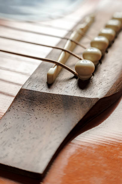 Bridge saddle with strings close-up, on an old acoustic guitar, under natural lighting..