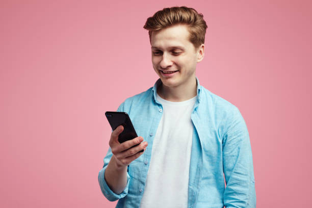 istock Positive smiling man smiling while holding smartphone, isolated over pink 1327462626