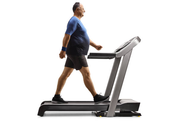 Full length profile shot of a mature man walking on a treadmill Full length profile shot of a mature man walking on a treadmill isolated on white background chubby arab stock pictures, royalty-free photos & images