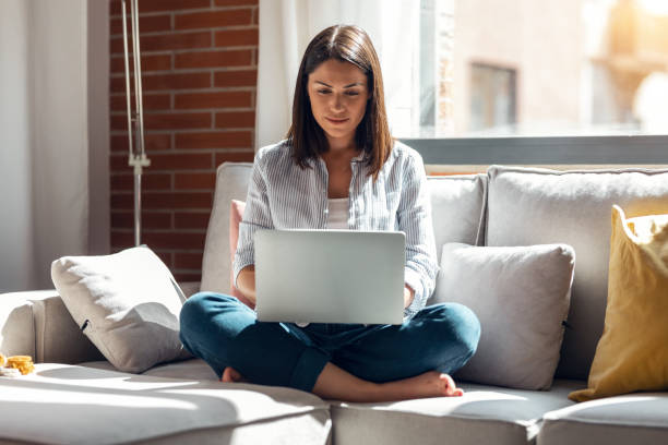 istock Pretty young woman working with her laptop while sitting on couch at home. 1327466742