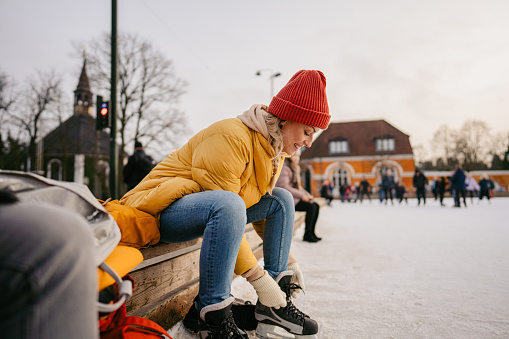 Photo of a young woman putting ice skates on as she is getting ready for ice skating.