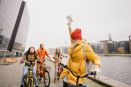 Photo of a tour guide giving directions to a small group of tourists while riding bikes and exploring the city; a tour guide introducing the culture, history, and architecture to people on organized sightseeing.