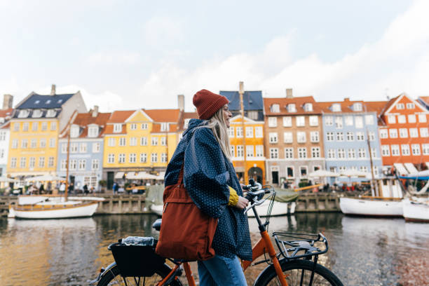 Sightseeing Photo of a young woman pulling the bike and walking down the street while exploring the famous tourist attraction in Copenhagen, Denmark. copenhagen stock pictures, royalty-free photos & images