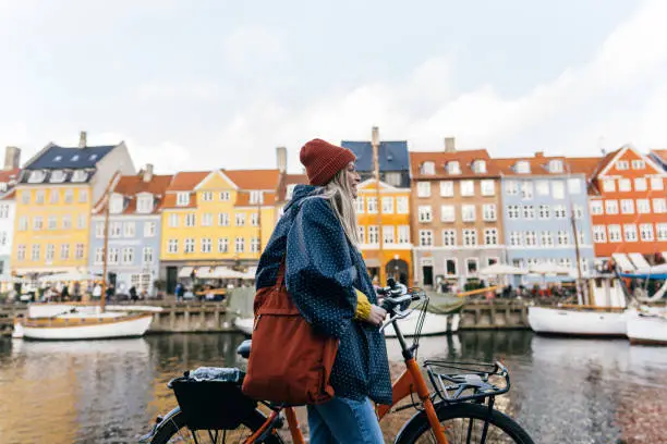 Photo of a young woman pulling the bike and walking down the street while exploring the famous tourist attraction in Copenhagen, Denmark.