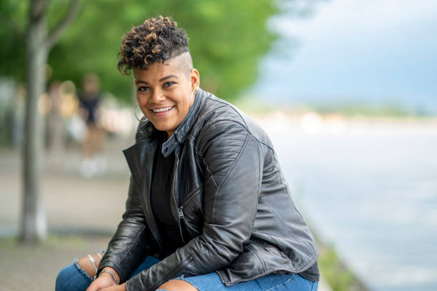 Smiling African American woman in the city A 32 year old woman laughs as she sits by the city waterfront. half shaved hairstyle stock pictures, royalty-free photos & images