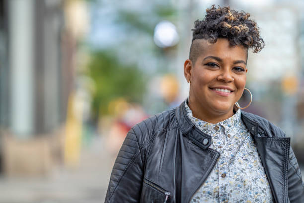 Cheerful, urban African American woman A 32 year old woman smiles at the camera as she stands on a sidewalk in the city. shaved black women stock pictures, royalty-free photos & images