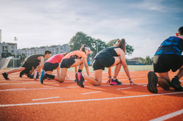 seitenansicht asiatische chinesische athleten, die sich auf die startlinie vorbereiten und morgens im leichtathletikstadion in richtung ziellinie laufen - mixed age stock-fotos und bilder