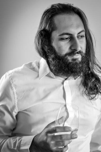 retrato de um jovem empresário do oriente médio com barba e cabelos longos segurando uma taça de vinho branco fresco - staring black and white glasses human face - fotografias e filmes do acervo