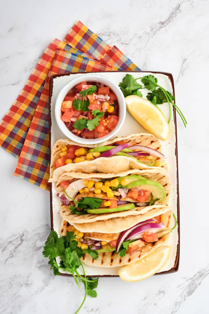 istock Mexican tacos with grilled chicken, avocado, corn kernels, tomato, onion, cilantro and salsa at white stone table. Traditional Mexican and Latin american street food. Top view. 1327481956