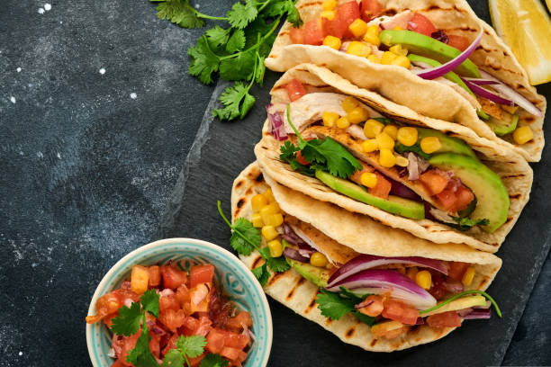 istock Mexican tacos with grilled chicken, avocado, corn kernels, tomato, onion, cilantro and salsa at black stone table. Traditional Mexican and Latin american street food. Top view. 1327482814