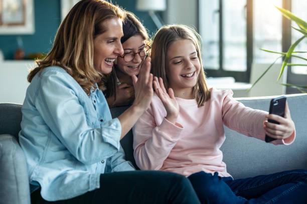 istock Happy mother and her little daughters making videocall with mobile phone while sitting together on couch at home. 1327482989