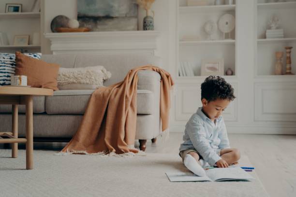 istock African cute boy calmly sitting on warm floor and playing with colored felt tip pens 1327485312