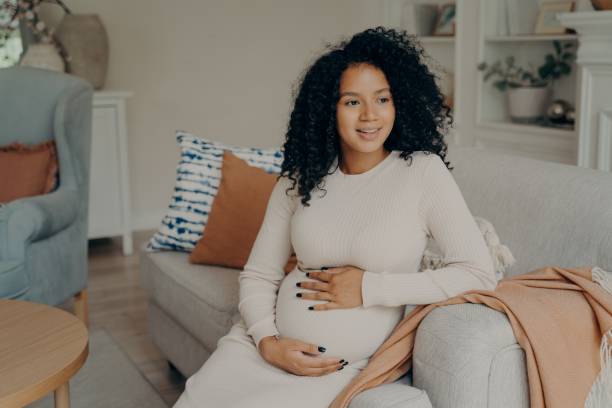 istock Smiling lovely african young future mom sitting on sofa 1327485380